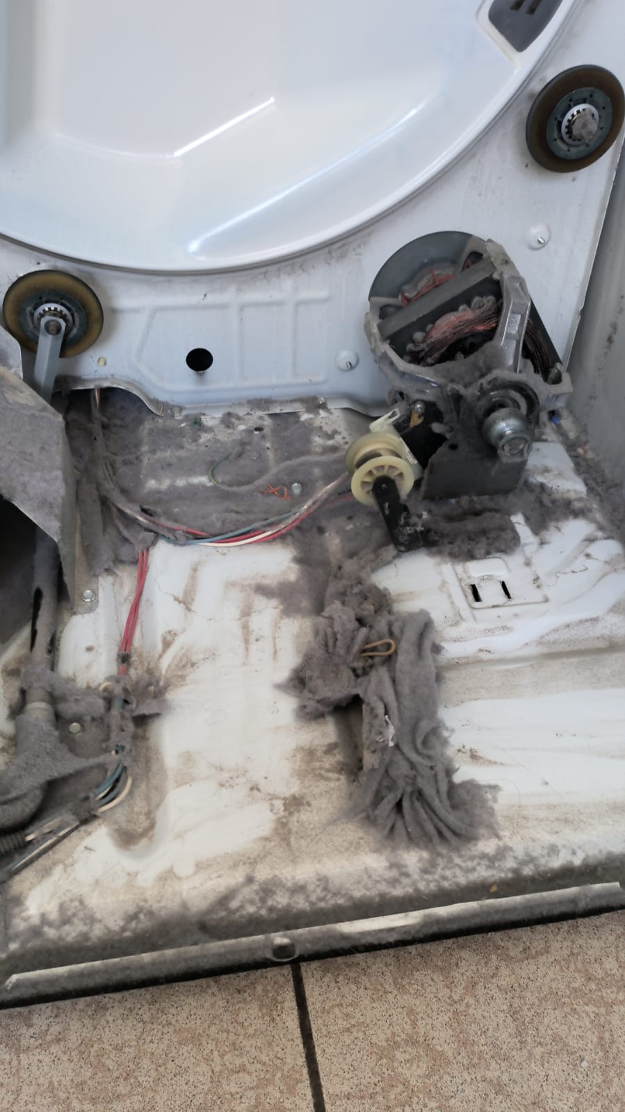 Interior de secadora lleno de pelusa acumulada alrededor del motor y la base antes del servicio