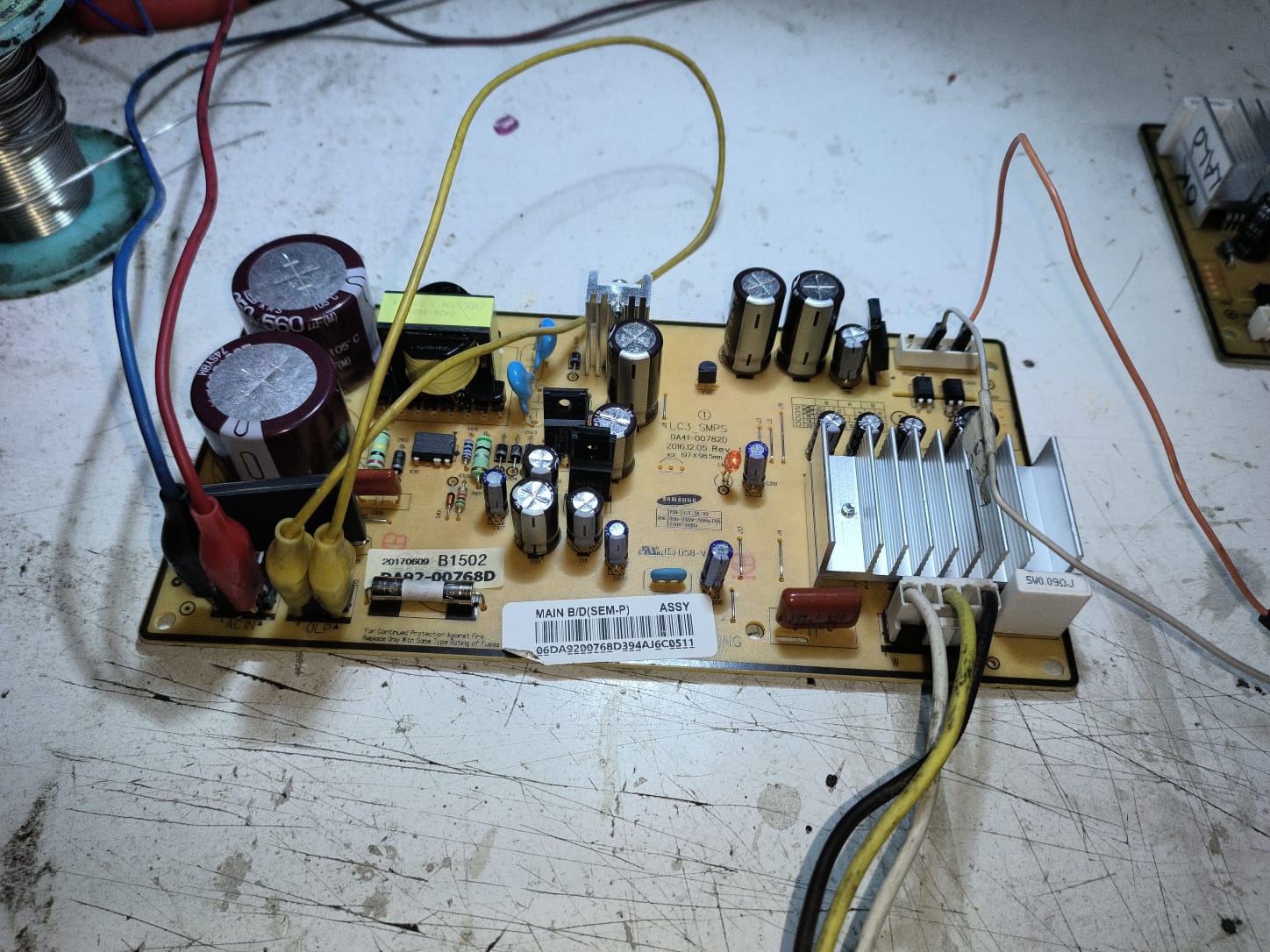 Tarjeta electrónica principal Samsung de refrigerador en el banco de pruebas con caimanes conectados para medir la fuente